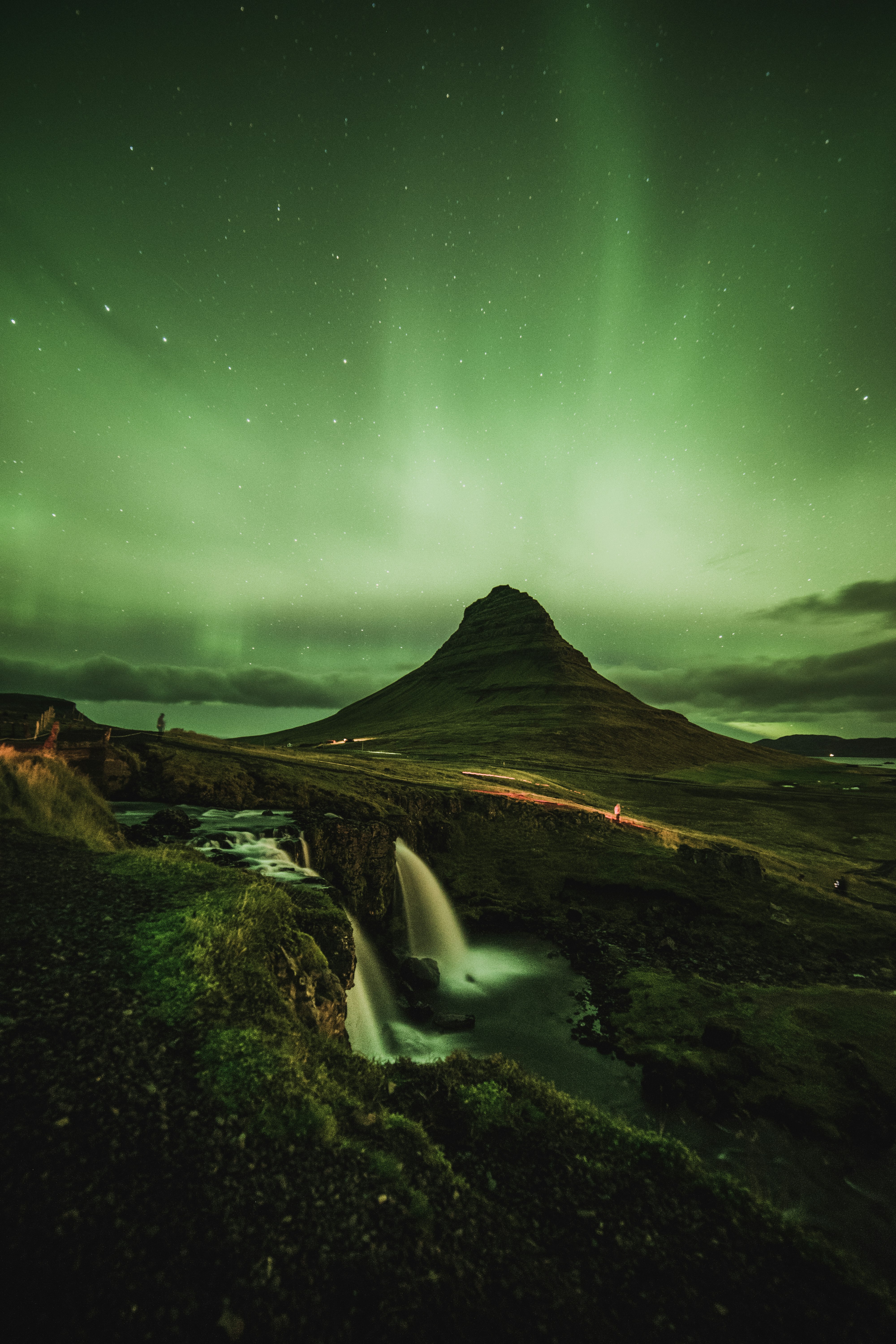 waterfalls near mountain taken under green sky